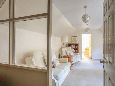 A sitting room with armchairs a wooden side table a floor lamp a bookshelf and two pendant lights at Glan Gors in Llanerchymedd