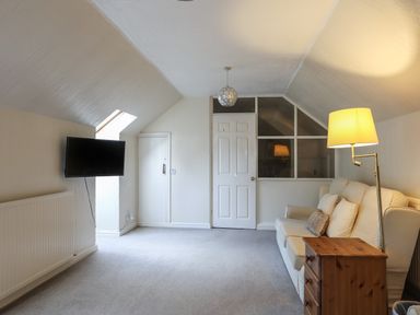 A sitting room with a sofa pillows floor lamp wooden chest of drawers wall-mounted television and a door at Glan Gors in Llanerchymedd