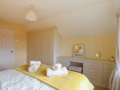 A bedroom with a bed with towels on a yellow throw and built-in wardrobes and a dressing table at Glan Gors in Llanerchymedd