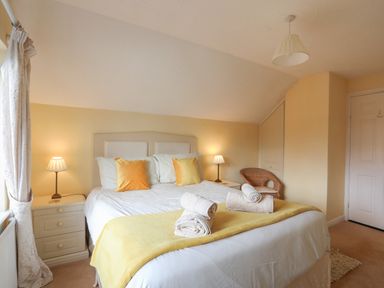 A bedroom with a double bed two bedside tables with lamps a wicker chair and a closed door at Glan Gors in Llanerchymedd