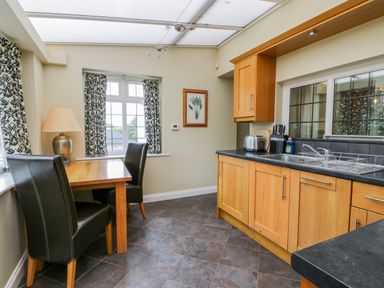A kitchen with wooden cabinets a black countertop a dining table with two black chairs and patterned curtains at Stakesby House Apartment 1 Whitby