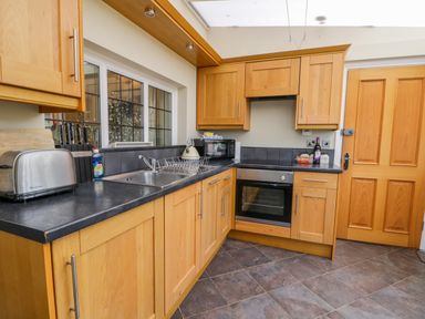 A kitchen with wooden cabinets a black countertop a toaster a sink with a drying rack a microwave an oven and a wooden door at Stakesby House Apartment 1 Whitby