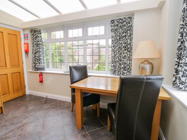 A dining area with a wooden table and two black chairs near patterned curtains and a window at Stakesby House Apartment 1 in Whitby