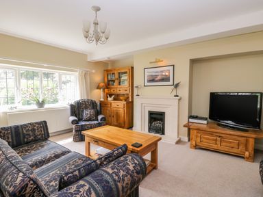 A living room with patterned sofa set wooden coffee table wooden cabinets fireplace and television at Stakesby House Apartment 1 Whitby