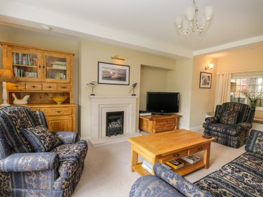 A living room with patterned armchairs wooden furniture a fireplace and a television at Stakesby House Apartment 1 in Whitby