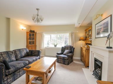 A living room with patterned sofa and armchair a wooden coffee table a fireplace and wooden cabinets at Stakesby House Apartment 1 in Whitby