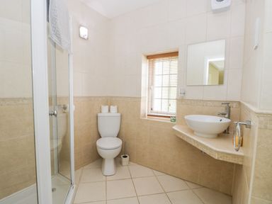 A bathroom with a shower, toilet, sink, mirror, and window at Stakesby House Apartment 1 in Whitby