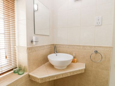 A bathroom corner with a round white sink on a tiled countertop a mirror soap dispenser and window blinds at Stakesby House Apartment 1 in Whitby