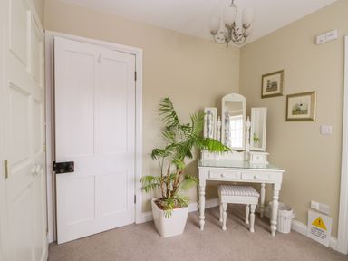 A room corner with a white dressing table and stool a green potted plant and framed pictures on beige walls at Stakesby House Apartment 1 in Whitby