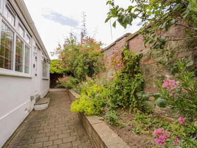 A brick paved pathway beside a white building with flower beds and a stone and brick wall at Stakesby House Apartment 1 in Whitby