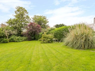 A garden with a lawn surrounded by trees shrubs and a small table with two chairs at Stakesby House Apartment 1 in Whitby