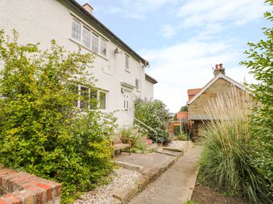 A pathway leading to a white house with plants and a wooden bench at Stakesby House Apartment 1 in Whitby