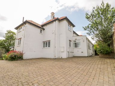 The exterior of a white two-story house with a tiled roof a paved driveway and surrounding trees and plants at Stakesby House Apartment 1 in Whitby