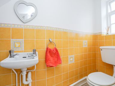 A bathroom with a white sink, a red towel hanging on a ring, a heart-shaped mirror, and a toilet with orange tiled walls at The Pink House in Rhosneigr