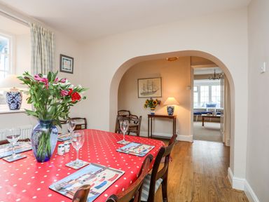 A dining room with a red polka dot tablecloth on the table flowers in a blue vase and an archway leading to another room at The Pink House in Rhosneigr
