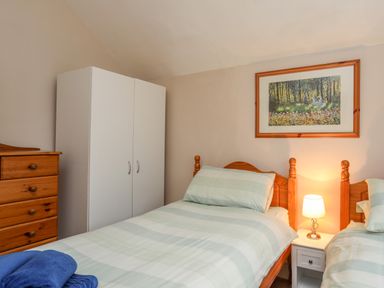 A bedroom with two single beds a white wardrobe a wooden chest of drawers and a lamp on a bedside table at The Pink House in Rhosneigr