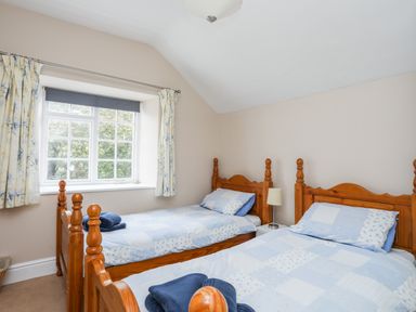 A bedroom with two single wooden beds two blue patterned bedspreads a window with curtains and a bedside table with a lamp at The Pink House in Rhosneigr