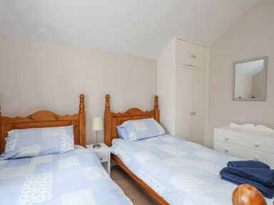 A bedroom with two single beds a nightstand with a lamp built in closet and dresser with mirror at The Pink House in Rhosneigr