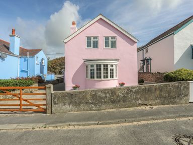 A pink house with white framed windows and a wooden gate next to a blue house at The Pink House in Rhosneigr