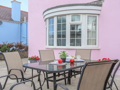 An outdoor patio with a black table and six chairs in front of a pink house with a bay window at The Pink House in Rhosneigr