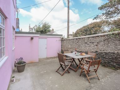 An outdoor patio with a wooden table and chairs next to a pink building and stone wall at The Pink House in Rhosneigr