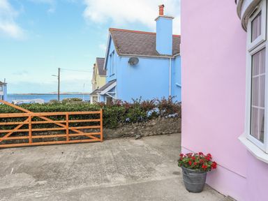 A pink house wall with flower pot in front and blue house with chimney and wooden gate near the sea at The Pink House in Rhosneigr