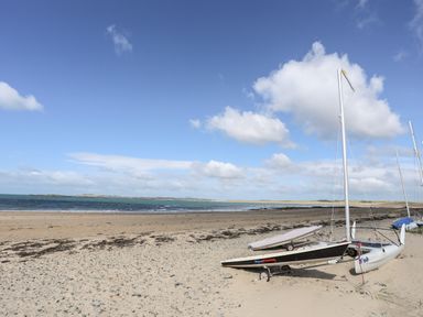 A sandy beach with small sailboats and a view of the sea at The Pink House in Rhosneigr