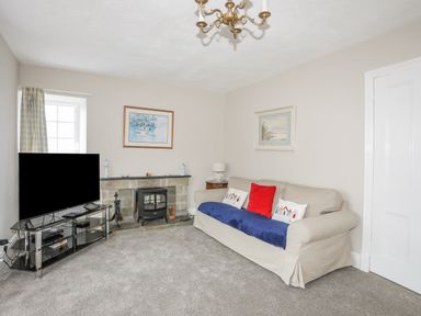 A living room with a sofa a television a fireplace and paintings on the walls at The Pink House in Rhosneigr