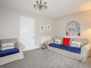 A living room with beige sofas and blue cushions a white door and shelf with plates at The Pink House in Rhosneigr