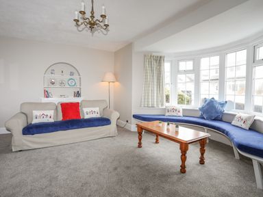 A living room with a beige sofa and blue cushions a wooden table and a blue window seat at The Pink House in Rhosneigr