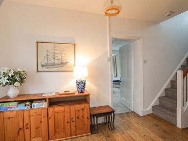A hallway with wooden cabinet lamp and flower vase next to carpeted stairs and open door at The Pink House in Rhosneigr