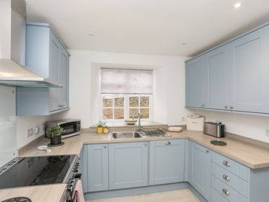 A kitchen with blue cabinets a stove a microwave a sink and countertop items at The Pink House in Rhosneigr