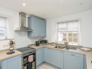 A kitchen with blue cabinets a stove a microwave and a sink at The Pink House in Rhosneigr