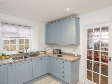 A kitchen with light blue cabinets a stainless steel sink toaster and glass paneled door at The Pink House in Rhosneigr