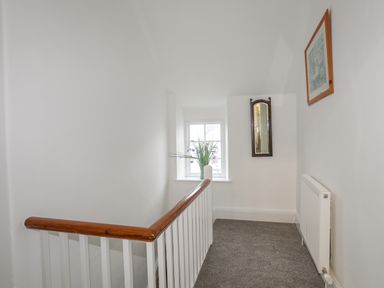 A stair landing with a wooden banister a window with flowers a wall mirror a painting and a radiator at The Pink House in Rhosneigr
