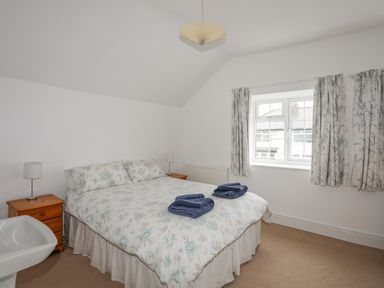 A bedroom with a double bed and floral bedding with nightstands and blue towels on the bed at The Pink House in Rhosneigr