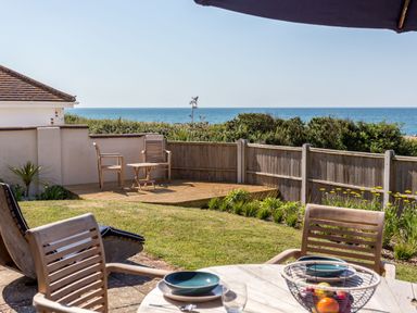 A garden with wooden chairs and table set with plates and glasses overlooking the sea at Beach Haven in West Bexington