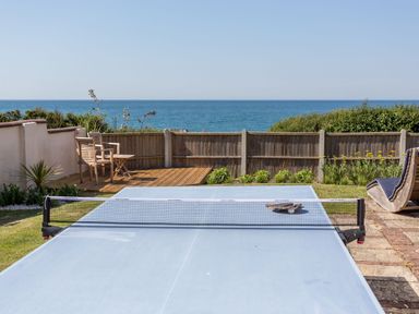 A backyard with a ping pong table chairs wooden deck and ocean view at Beach Haven in West Bexington