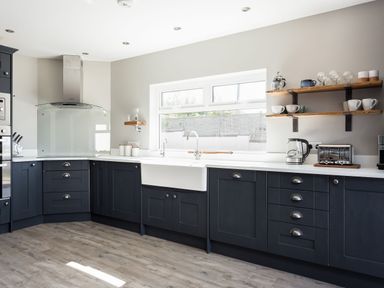 A kitchen with dark cabinets white countertops a farmhouse sink and open shelves holding mugs and glasses at Beach Haven in West Bexington