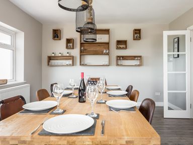 A dining room with a wooden table set with plates glasses and a bottle of wine and wooden shelves on the wall at Beach Haven in West Bexington
