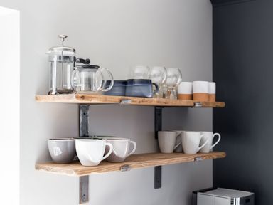 Two wooden shelves holding coffee mugs glass cups and tea pots in a kitchen at Beach Haven in West Bexington