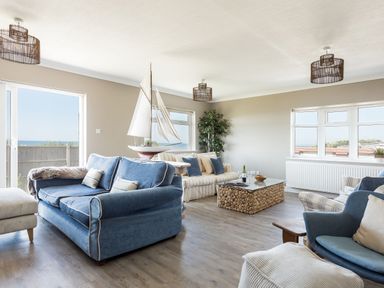 A living room with blue and striped sofas a wine bottle on a coffee table and ocean views at Beach Haven in West Bexington
