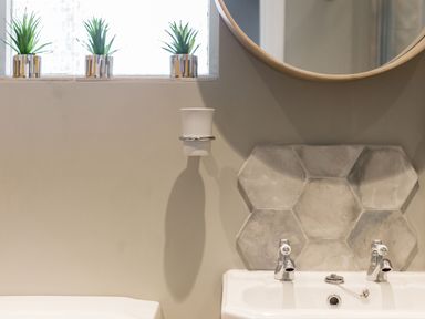 A bathroom sink with hexagonal tiles behind taps and three small plants on a window sill at Beach Haven in West Bexington