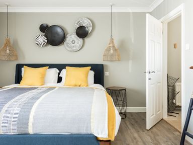 A bedroom with a bed with yellow pillows and blanket a side table pendant lights and wall decorations at Beach Haven in West Bexington