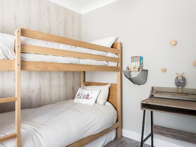 A bedroom with wooden bunk beds and a small desk with wall shelf and decorations at Beach Haven in West Bexington