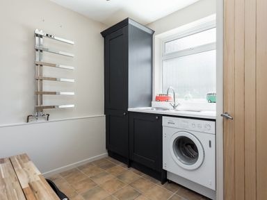 A utility room with a washing machine black cabinets a stainless steel towel radiator and a window at Beach Haven in West Bexington