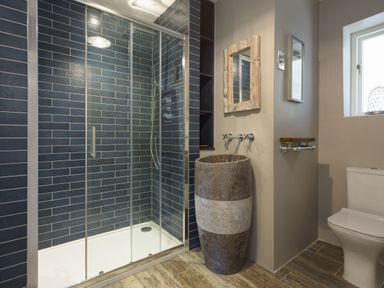 A bathroom with a glass shower enclosure blue tiled walls a stone sink wooden floor and a toilet at Beach Haven in West Bexington