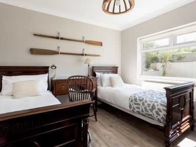 A bedroom with two single beds a wooden desk and chair and paddles on the wall at Beach Haven in West Bexington