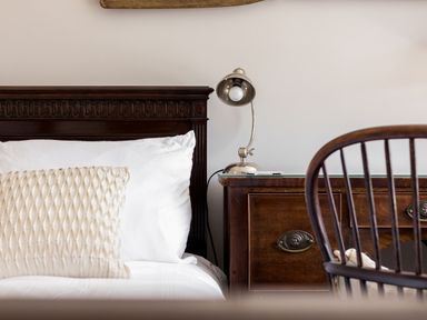 A bed with white pillows and a beige cushion next to a wooden nightstand with a silver lamp and a wooden chair at Beach Haven in West Bexington