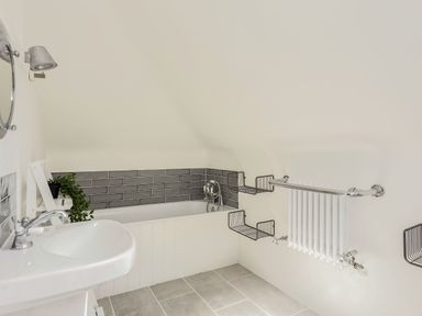 A bathroom with a bathtub sink wall-mounted mirror and towel radiator at Beach Haven in West Bexington